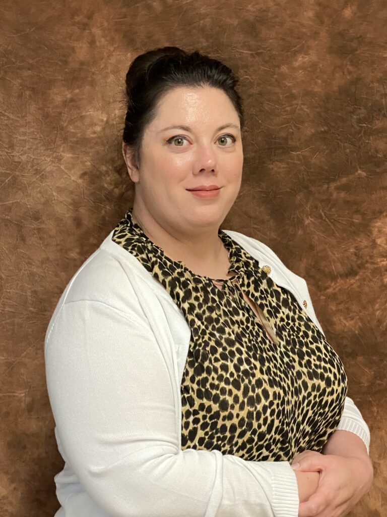 White woman with dark brown hair pulled into a bun, wearing a white cardigan and leopard print blouse