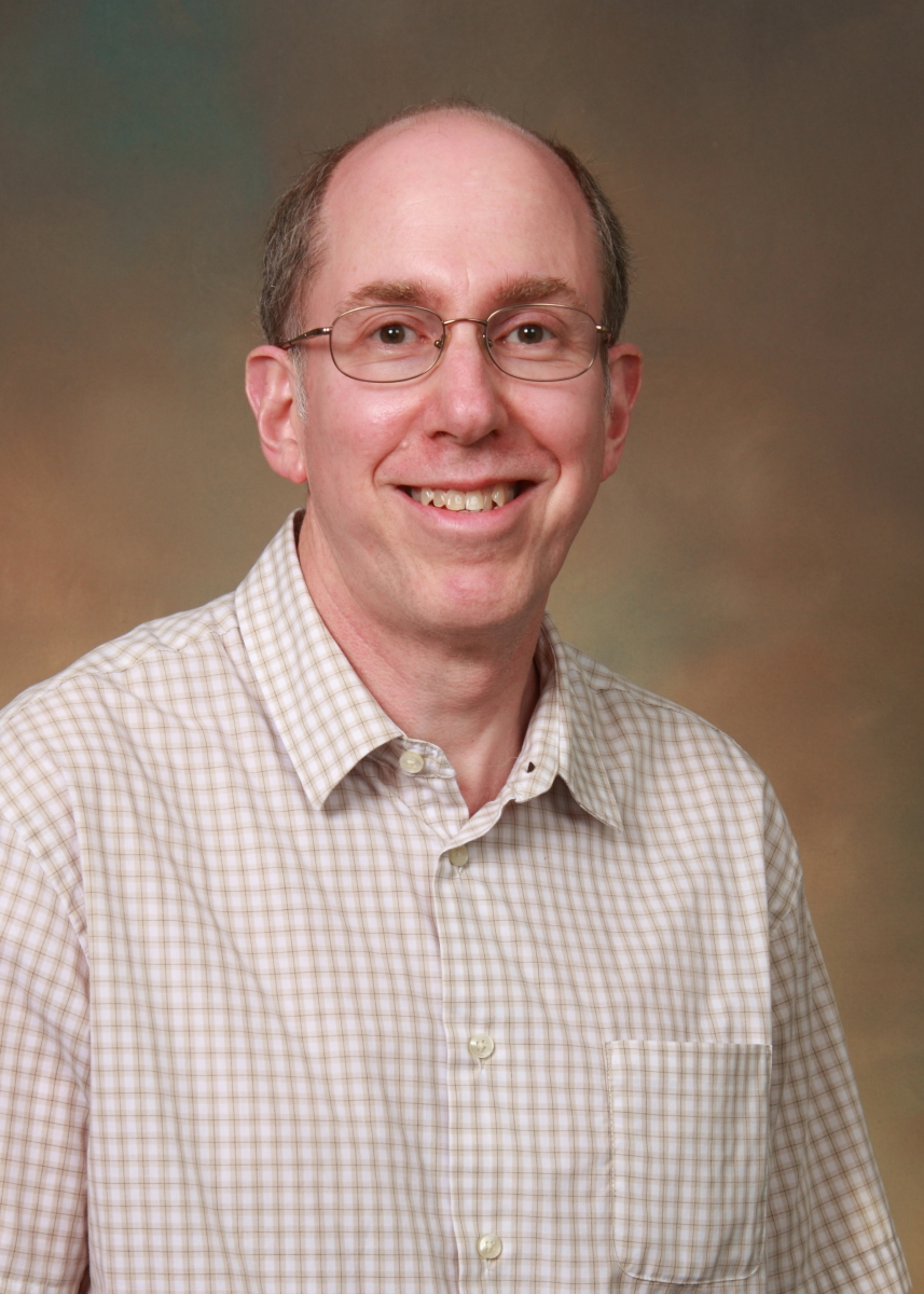 white man with thin light brown/reddish hair wearing glasses and a white and grey checkered button up collared shirt