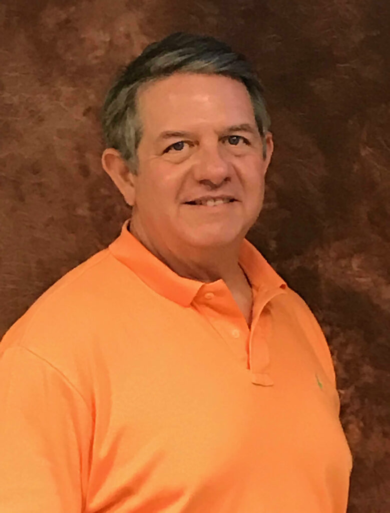 white man with greying dark brown hair wearing an orange polo