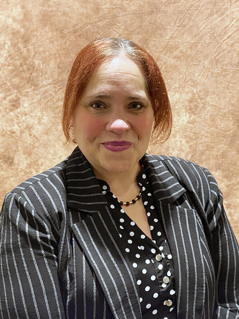 Latina woman with red hair wearing a polka dot blouse and striped suit jacket